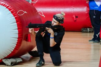Игрок LASERWAR в низкой стойке с оружием у красного препятствия.